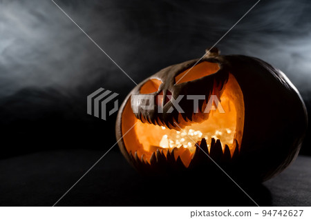 A creepy pumpkin with a carved grimace in the smoke. Jack o lantern in the dark. 94742627