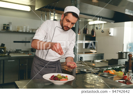 Chef sprinkles salt to salad of fresh vegetables in kitchen of restaurant. Tasty and healthy food 94742642