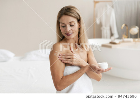 Body treatments. Happy middle aged woman applying moisturising cream on shoulder, making beauty care routine 94743696