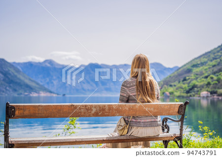 A woman sits on a bench and admires the view of the Bay of Kotor. Montenegro 94743791