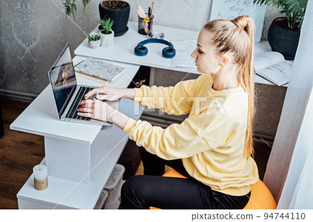 Sitting on gym ball at work. Use exercise ball like chair at workplace. Freelancer woman sitting on orange fitness ball using laptop in home office 94744110