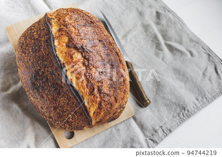 Round fresh bread lies on the cutting board. Baking and confectionery in a bakery or restaurant. Round fresh bread lies on the cutting board. Baking and confectionery in a bakery or restaurant. 94744219