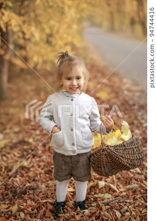 Cute girls with basket full of yellow dry fallen leaves Cute girls with basket full of yellow dry fallen leaves 94744416