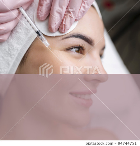Close up of hands of young cosmetologist injecting botox in female face. She is standing and smiling. The woman is closed her eyes with relaxation Close up of hands of young cosmetologist injecting botox in female face. She is standing and smiling. The woman is closed her eyes with relaxation 94744751