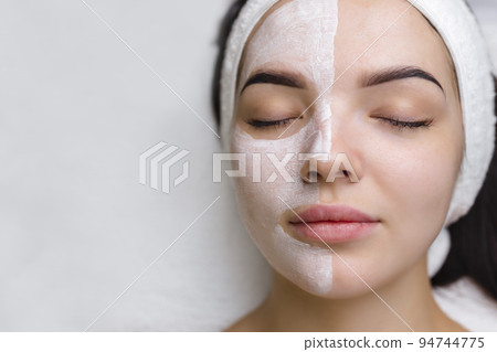 Close-up shot of a woman getting facial treatment with clay mask. Cosmetology and spa 94744775