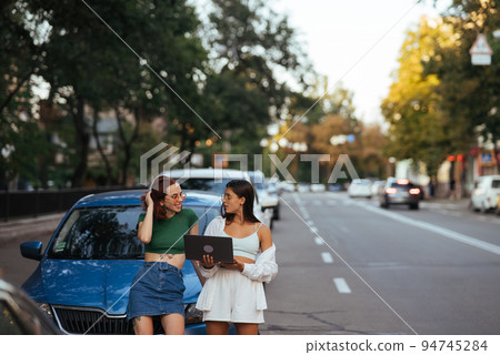 Two young women with a laptop near the car Two young women with a laptop near the car 94745284