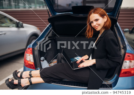 Woman working on laptop while sitting in trunk of car 94745319