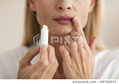 Attractive mature woman applying lipstick and touching lips, moisturizing skin, closeup shot, cropped Attractive mature woman applying lipstick and touching lips, moisturizing skin, closeup shot, cropped 94746974