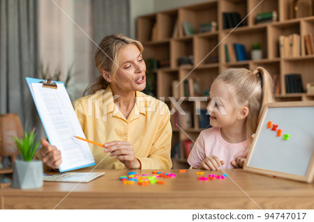 Professional female teacher exercising with clever preschool girl, little child counting and repeating words and numbers 94747017