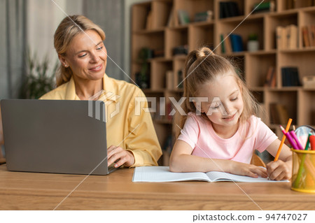 Cheerful mother using laptop, working remotely and spending time together with daughter, cute little girl drawing Cheerful mother using laptop, working remotely and spending time together with daughter, cute little girl drawing 94747027