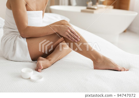Unrecognizable middle aged woman sitting on bed at home and moisturizing her skin on legs, cropped, copy space Unrecognizable middle aged woman sitting on bed at home and moisturizing her skin on legs, cropped, copy space 94747072