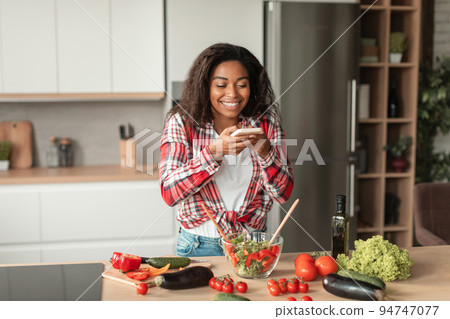 Cheerful millennial african american woman make photo of salad with organic vegetables, enjoy cooking meal Cheerful millennial african american woman make photo of salad with organic vegetables, enjoy cooking meal 94747077