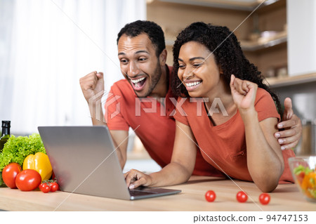 Glad millennial african american family at table with organic vegetables uses laptop, make victory gesture 94747153