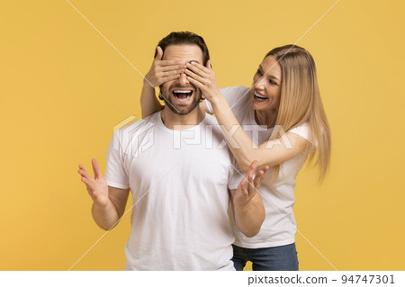 Smiling young caucasian woman in white t-shirt closes eyes to shocked man with open mouth 94747301