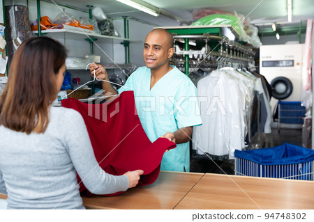 Man dry-cleaning worker giving clothes to customer 94748302