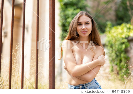Portrait of half-naked young woman on city street near wrought iron fence 94748509