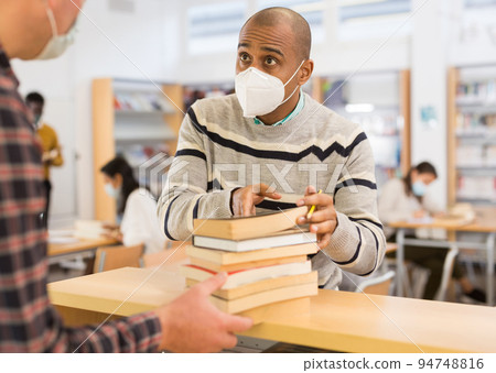 Man in mask returning books at library Man in mask returning books at library 94748816