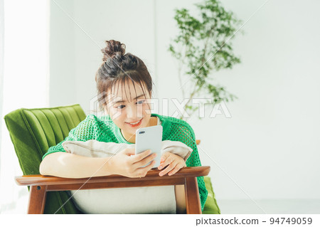 A woman lying on the sofa and looking at her smartphone A woman lying on the sofa and looking at her smartphone 94749059