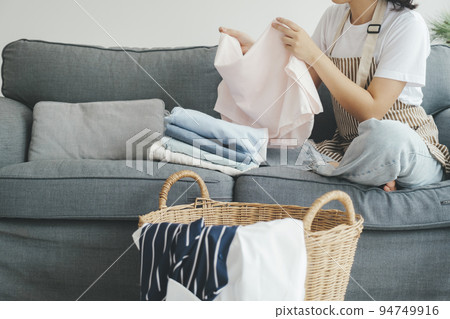 Young woman folding clothes on sofa at home. 94749916