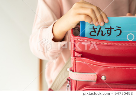 Elementary school student taking out a math notebook from a school bag 94750498
