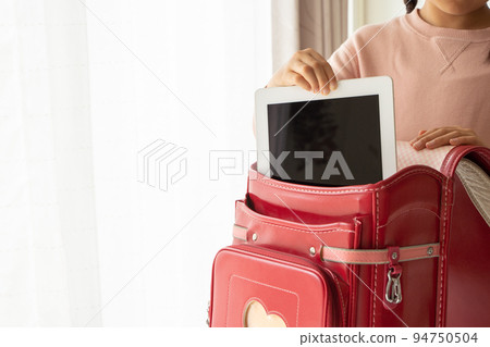 Elementary school student taking out a tablet device from a school bag 94750504