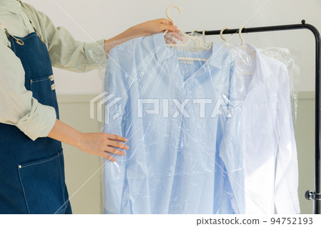 aesthetic laundry concept_person checking the rack with clean shirts in plastic bags after dry cleaning 94752193