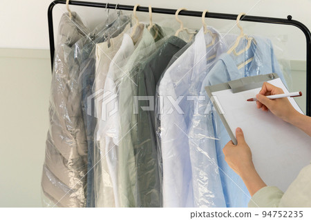 aesthetic laundry concept_person checking the rack with clean shirts in plastic bags after dry cleaning 94752235