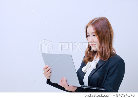 一個站著打開電腦,看著屏幕的年輕女人 一個站著打開電腦,看著屏幕的年輕女人 94754176