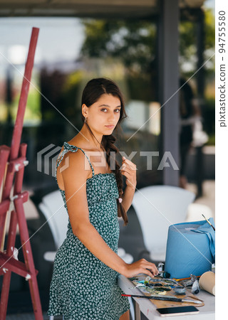 Young woman artist stands close table with a palette Young woman artist stands close table with a palette 94755580
