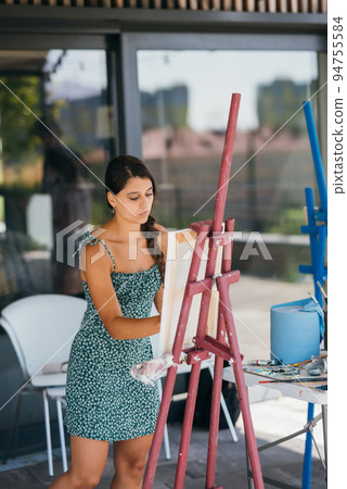 Young woman artist paints with a spatula on the canvas Young woman artist paints with a spatula on the canvas 94755584