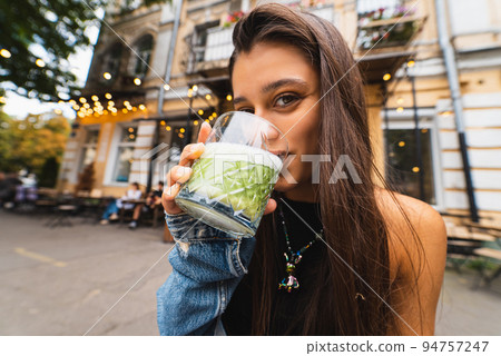 Woman holding glass cup of tasty smoothie and drinking, outdoors 94757247