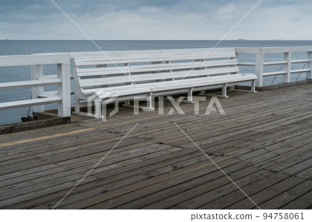 Empty bench on wooden boardwalk at seashore 94758061
