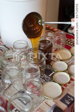 Filling of glass jars of honey on a table 94759956