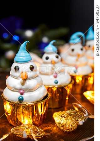 Christmas cakes in the shape of snowmen on a background of glowing garlands 94760237