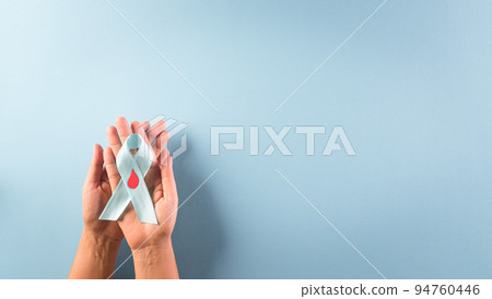 World diabetes day awareness concept. Hand holding blue ribbon, symbolic bow color raising awareness in diabetes day on pastel background, 14 November. World diabetes day awareness concept. Hand holding blue ribbon, symbolic bow color raising awareness in diabetes day on pastel background, 14 November. 94760446