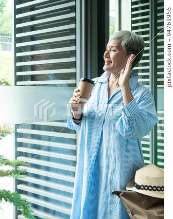 一位 60 歲的亞洲成熟女性戴著紙杯喝茶或喝咖啡,等待旅行或觀光的概念。 一位 60 歲的亞洲成熟女性戴著紙杯喝茶或喝咖啡,等待旅行或觀光的概念。 94761956