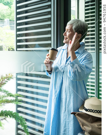 一位 60 歲的亞洲成熟女性戴著紙杯喝茶或喝咖啡，等待旅行或觀光的概念。 94761958