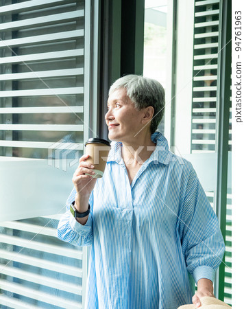 一位 60 歲的亞洲成熟女性戴著紙杯喝茶或喝咖啡，等待旅行或觀光的概念。 94761963