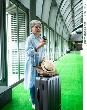 一位 60 歲的亞洲成熟女性戴著紙杯喝茶或喝咖啡,等待旅行或觀光的概念。 一位 60 歲的亞洲成熟女性戴著紙杯喝茶或喝咖啡,等待旅行或觀光的概念。 94761967