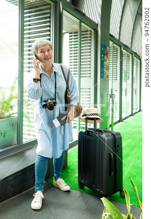 60多歲的亞洲熟年婦女微笑著站在身旁有手提箱行李袋和使用智能手機,適用於covid19疫情後旅行的概 94762002