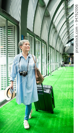 Asian mature woman in her 60s smiling and standing with suitcase duffel bag and holding straw hat, concept for travel after covid19 epidemic 94762006