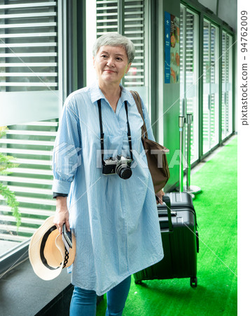 60多歲的亞洲熟年婦女微笑著站著,身旁有手提箱行李袋和手持草帽,適用於covid19疫情後旅行的概念 94762009