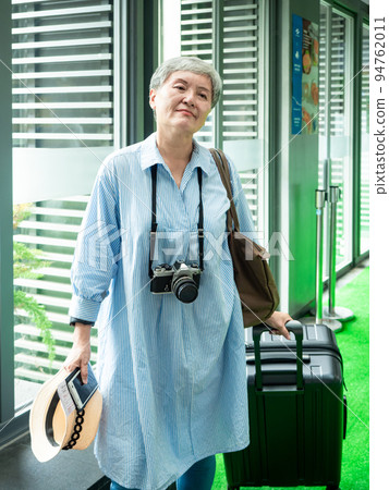 60多歲的亞洲熟年婦女微笑著站著,身旁有手提箱行李袋和手持草帽,適用於covid19疫情後旅行的概念 94762011