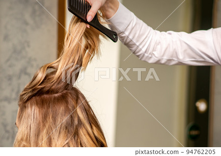 Professional hair care. Young female blonde with long hair receiving hairstyling in a beauty salon Professional hair care. Young female blonde with long hair receiving hairstyling in a beauty salon 94762205
