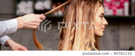 Professional hair care. Beautiful young caucasian blonde woman with long hair receiving hairstyling in a beauty salon Professional hair care. Beautiful young caucasian blonde woman with long hair receiving hairstyling in a beauty salon 94762210