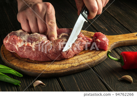 Butcher or chef cuts raw beef meat on a cutting board before baking. Hotel menu recipe idea Butcher or chef cuts raw beef meat on a cutting board before baking. Hotel menu recipe idea 94762266