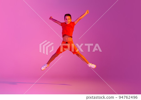 Happiness. Emotional kid in casual bright clothes jumping isolated over pink background in neon. Action, dance, happy childhood 94762496
