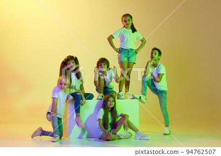 Fashionable kids. Group of children, little girls and boys in sportive casual style clothes isolated on green background in yellow neon light. Fashionable kids. Group of children, little girls and boys in sportive casual style clothes isolated on green background in yellow neon light. 94762507