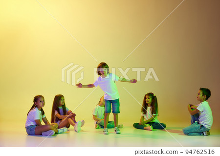 Stylish children, little girls and boys in casual style clothes dancing hip-hop isolated on green background in yellow neon light. Stylish children, little girls and boys in casual style clothes dancing hip-hop isolated on green background in yellow neon light. 94762516
