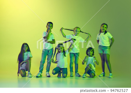 Group of children, little girls and boys in sportive casual style clothes dancing isolated on green background in yellow neon light. 94762527